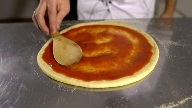 Koch-Hand-breitet-pasteurisierten-Tomatenpaste-auf-einen-Pizzateig-schließen,-sich