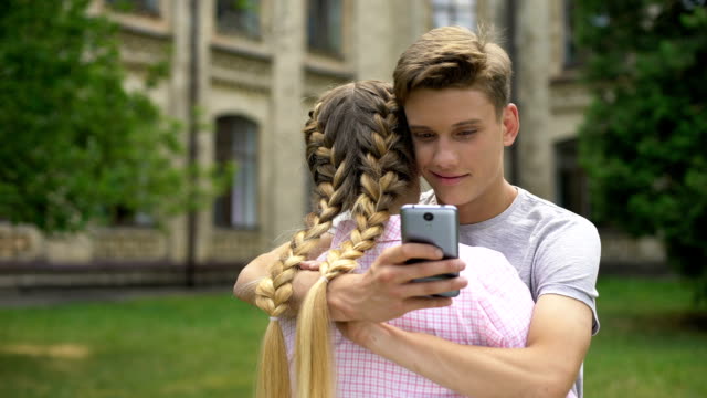 Teenager-using-cell-phone-while-hugging-boyfriend,-absorbed-by-social-networks