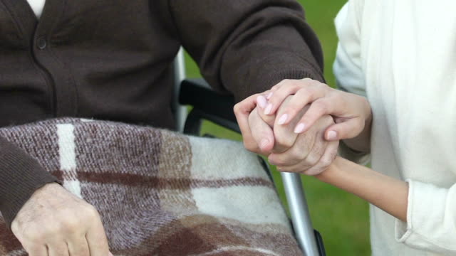 Woman-holding-hand-of-patient-in-wheelchair,-volunteer-program,-charity-concept
