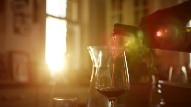 Man-Pouring-Red-Wine-Into-Glass-At-Kitchen-Table