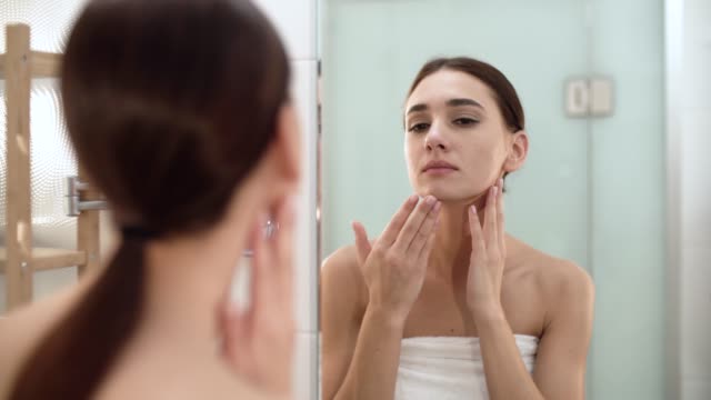 Pflege-der-Haut.-Frau-Gesicht-berühren-und-Blick-auf-den-Spiegel-im-Badezimmer