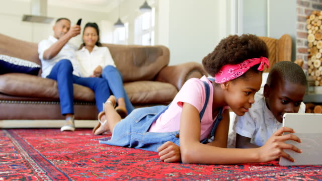 Vorderansicht-des-schwarzen-Kindern-auf-dem-Boden-liegend-und-mit-digital-Tablette-in-einem-komfortablen-Haus-4k