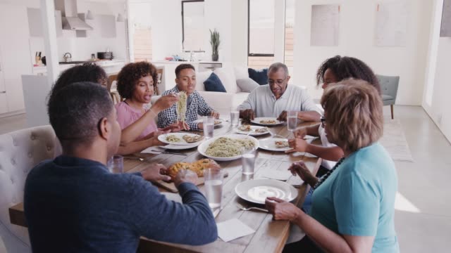 Three-generation-black-family-sitting-at-dinner-table-serving-spaghetti,-elevated-view