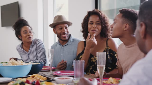 Familia-negra-de-tres-generaciones-sentadas-juntas-en-la-mesa-hablando-durante-una-celebración-familiar