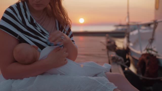 Mutter-stillt-und-streichelt-Baby-sitzen-auf-dem-Pier-bei-Sonnenuntergang