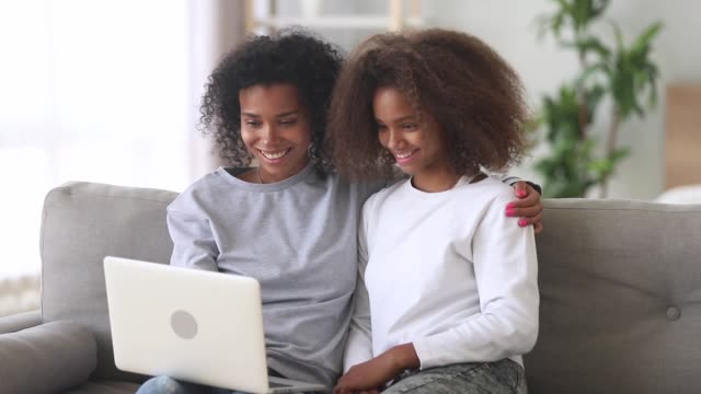 Mixed-race-mother-daughter-watching-movie-on-laptop-at-home