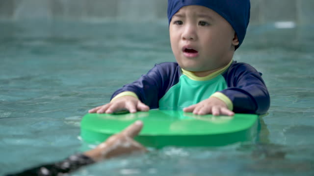 Madre-enseñando-niño-nadar-en-una-piscina.-El-niño-está-asustado-y-caminando-en-el-agua-a-mamá.