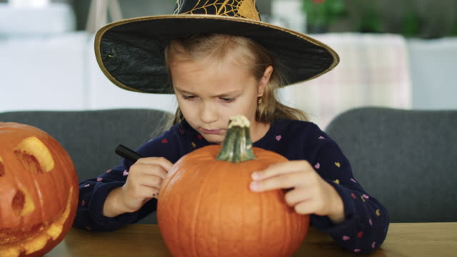 Girl-in-halloween-costume-drawing-on-pumpkin