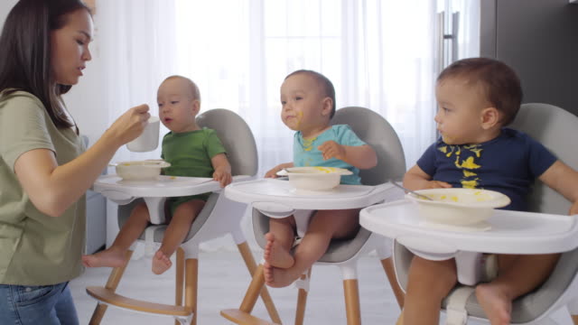 Asiatische-Mutter-Fütterung-Kleinkind-Triplets-in-Hochstühlen