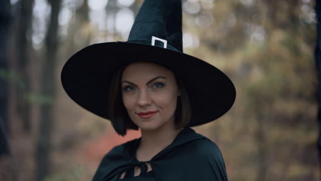 Beautiful-witch-in-cap,-long-dress,-mantle-on-autumn-forest-background.-Halloween-concept,-cosplay-dressing-up.-Slow-motion