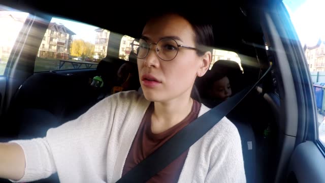 Frau-fährt-Auto-und-im-Gespräch-mit-Kindern-sitzen-auf-dem-Rücksitz
