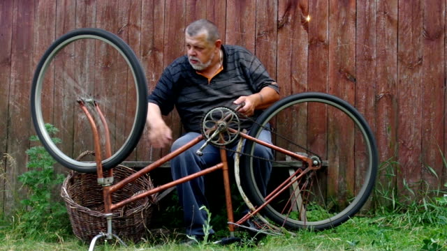 Mann-ist-nervös-über-sehr-altes-Fahrrad-zu-reparieren-sitzen-gegen-Holzzaun