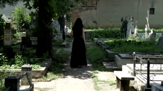 Creepy-woman-walking-in-cemetery-alley-to-beloved-grave-and-placing-a-crown-on-grave