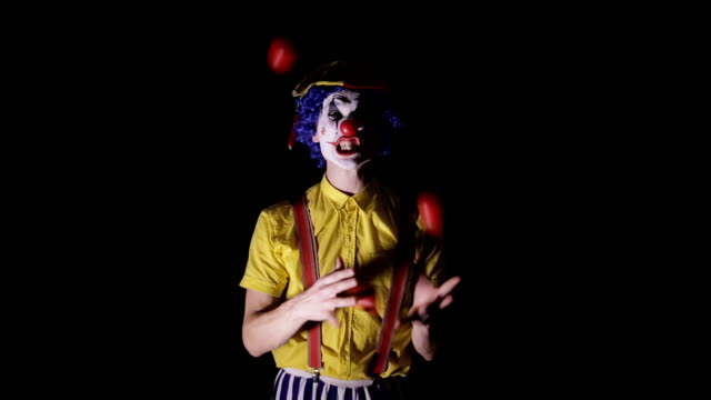 Ein-Clown-jongliert-rote-Äpfel-und-zeigt-die-Zähne.