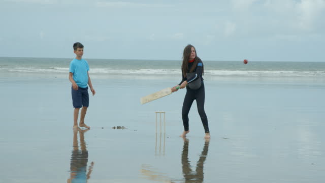 Dos-niños-jugando-Cricket-de-playa,-la-chica-de-bateo-golpea-el-balón.