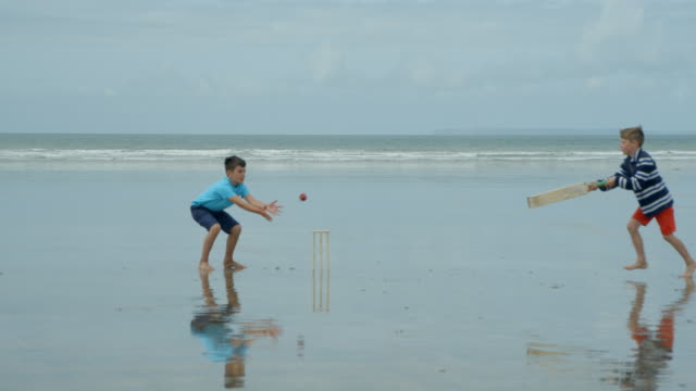 Zwei-Jungen-spielen-Strand-Cricket-einen-versuchen-zu-bekommen-und-die-anderen-Hits-die-Stümpfe!