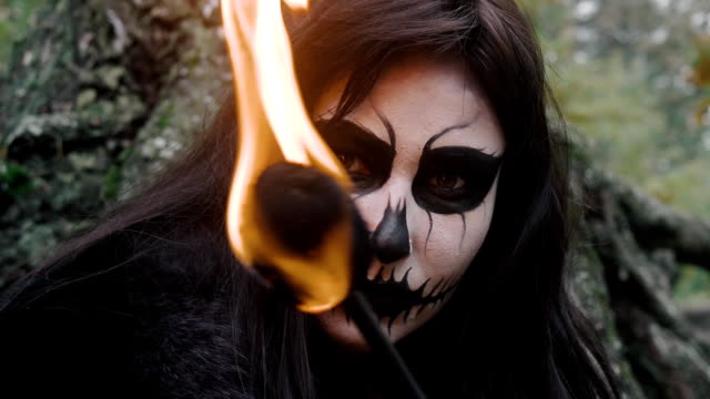 Young-woman-in-scary-black-and-white-halloween-make-up-and-fire-torch-looking-into-camera