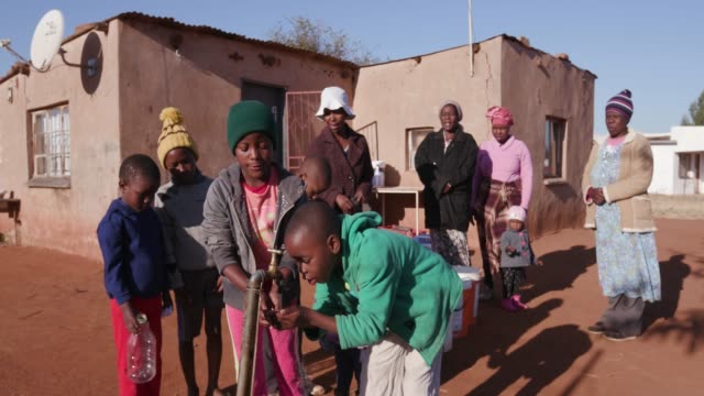 Young-african-boys-drinking-water-from-a-tap-while-woman-line-up-to-collect-water-in-plastic-containers-due-to-severe-drought-in-South-Africa