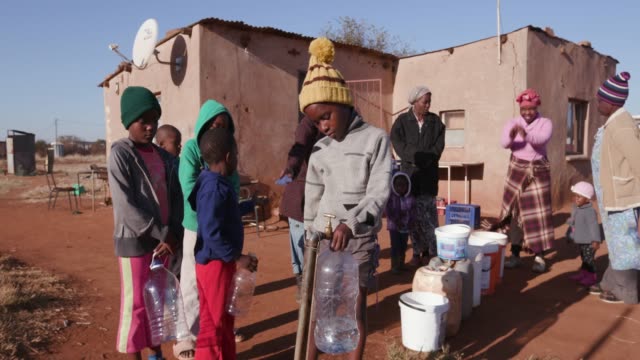 Young-african-boy-collecting-water-from-a-tap-while-woman-and-children-line-up-to-collect-water-in-plastic-containers-due-to-severe-drought-in-South-Africa