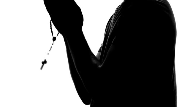 Religious-person-praying,-male-silhouette-holding-rosary-in-hand,-hope-and-faith