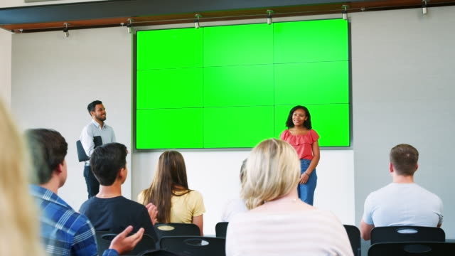 Female-Student-Giving-Presentation-To-High-School-Class-In-Front-Of-Screen
