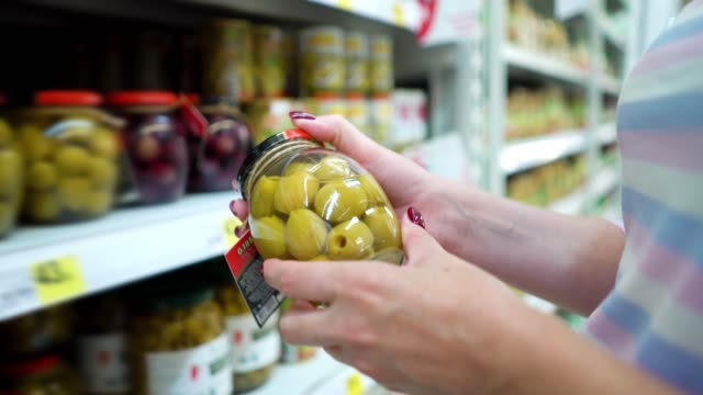 Closeup-caucasian-woman-hands-near-shop-shelves-choosing-marinade-green-olives-in-grocery-market