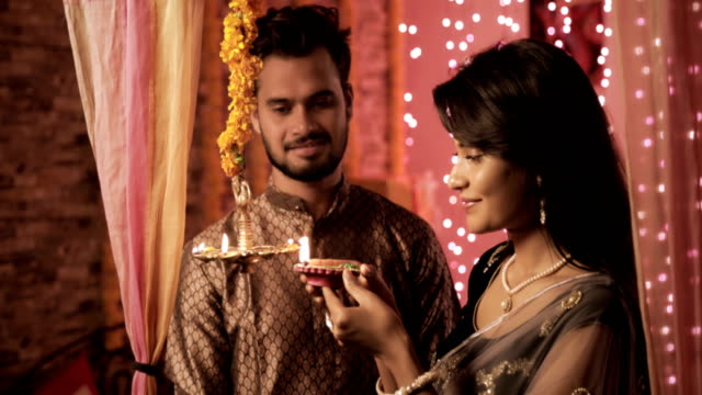 attraktive-Frau-trägt-Sari-leuchtet-eine-Öllampe-während-Diwali-fest,-während-Mann-trägt-Kurta-mit-einem-Lächeln-blickt-auf