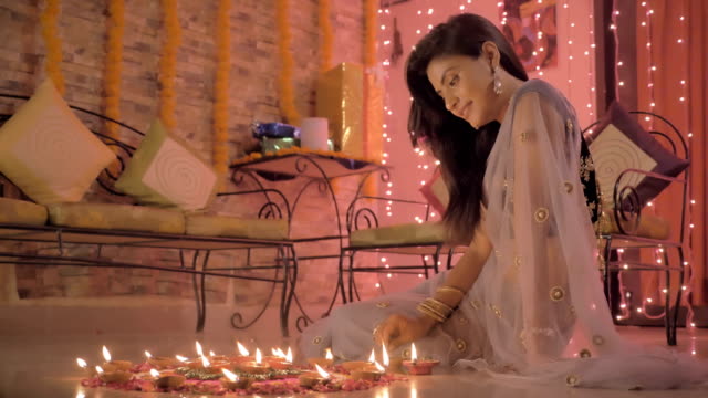 Una-hermosa-chica-en-adornos-haciendo-un-Rangoli-en-un-piso-durante-el-festival-de-Diwali-y-tradicional-sari.-Una-señora-sonriente-dibujando-arte-indio-en-el-piso-con-pétalos-de-flores,-de-color-arena-y-aceite-de-las-lámparas