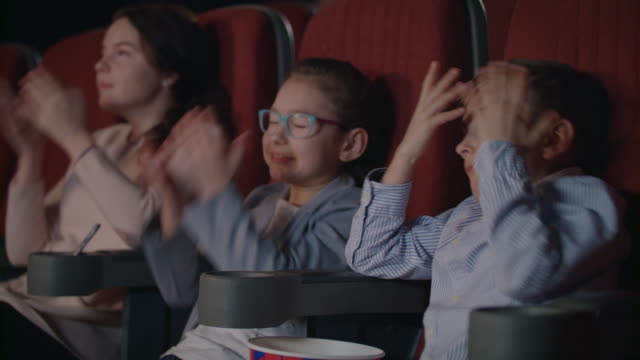 Kids-are-frightened-at-movie-theatre.-Scared-children-cover-faces-by-hands.