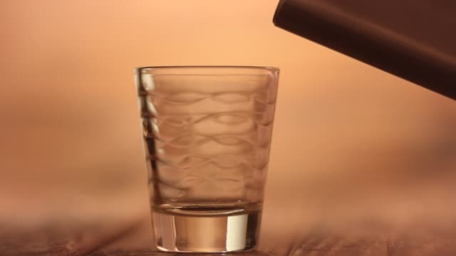 Pouring-a-whiskey-shot-on-a-shot-glass-using-a-metal-hip-alcohol-flask,-closeup-macro
