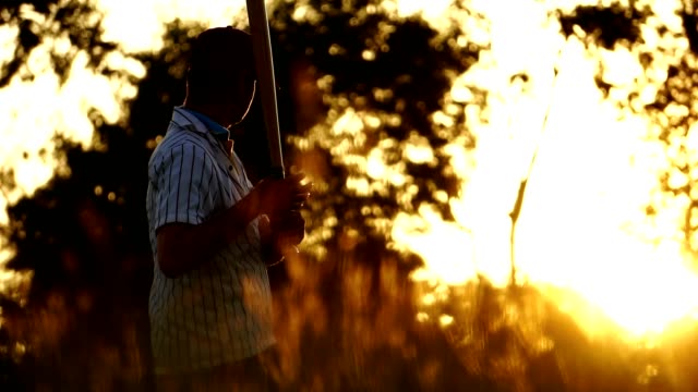 Herren-Baseball-Praxis-schlagen-einen-Baseball-mit-dem-Licht-des-Sonnenuntergangs