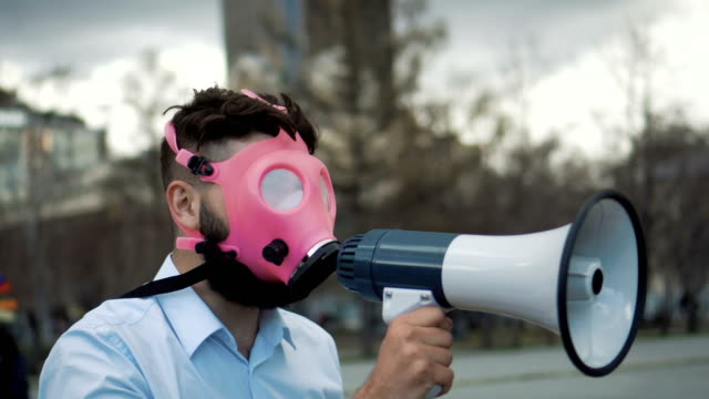 Kaukasischen-Mann-in-einer-rosa-Gasmaske-schreit-in-einem-Megaphon-Closeup.-Umweltverschmutzung-zu-stoppen