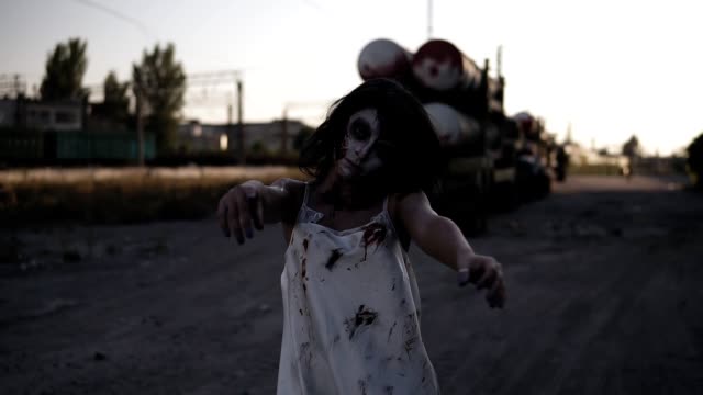 Creepy-zombie-woman-with-wounded-face-walking-outdoors-with-an-industrial-abandoned-place-on-the-background.-Halloween,-filming,-creepy-concept