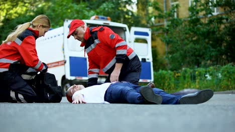 Tripulación-de-la-ambulancia-al-hombre-acostado-en-el-camino,-primeros-auxilios-en-la-escena-del-accidente-de-coche