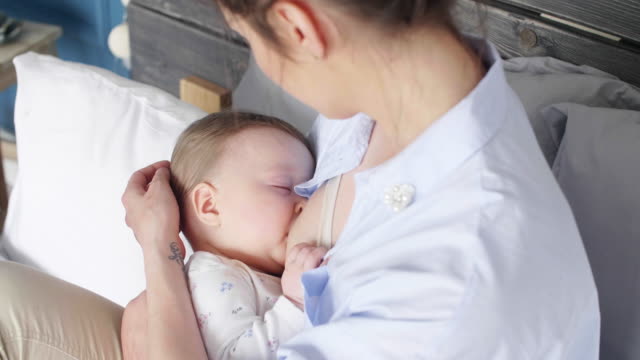 Affectionate-mother-breastfeeding-her-baby-girl-at-bedroom