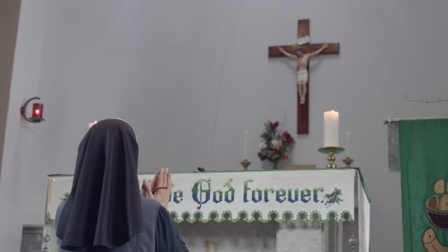 Ordensschwester-hält-Rosenkranz-und-kniend-vor-Altar.