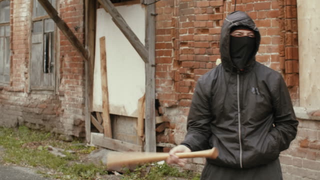 Hooliganin-schwarze-Maske-und-Jacke-mit-Kapuze-hält-in-Baseballschläger-auf-Straße