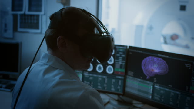Concepto-futurista:-En-Control-sala-médico-usa-casco-de-realidad-Virtual-supervisa-a-pacientes-sometidos-a-procedimiento-de-tomografía-computarizada-o-MRI.-Modelo-de-ordenador-muestra-Mostrar-cerebro-3D-con-posible-Tumor.