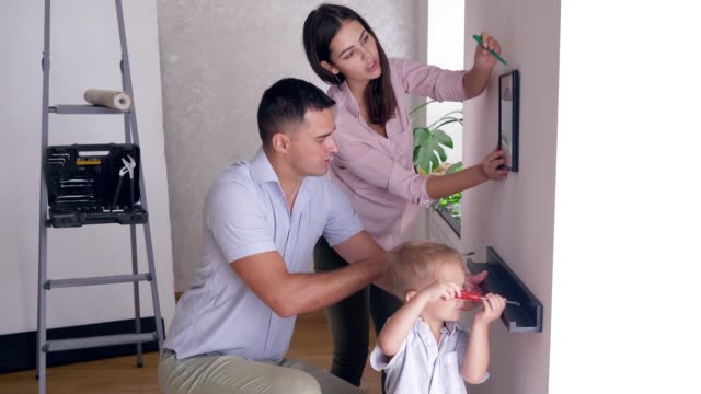 freundliche-Familie-mit-Kleinkind-Jungen-tun-renovieren-und-Schrauben-Regal-und-Bild-an-Wand