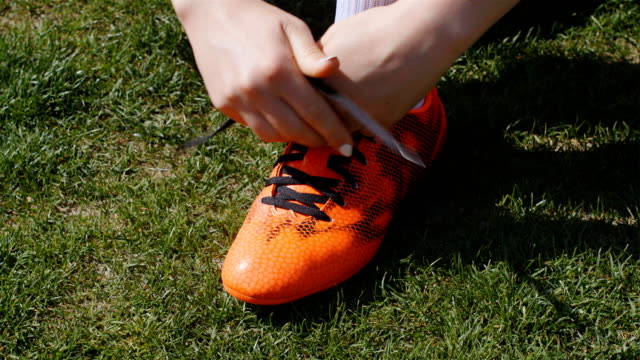Football,-soccer-game.-Professional-footballer-young-woman-buckle-her-red-shoes-before-training,-4k
