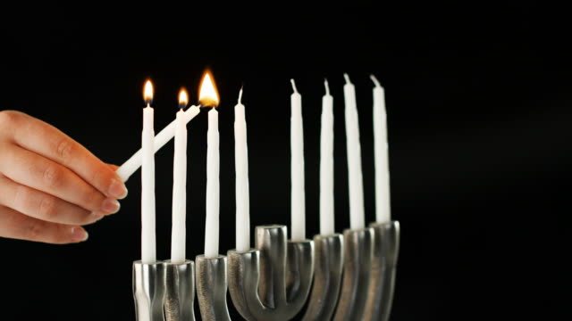 Hand-lighting-the-nine-white-candles-in-a-Jewish-menorah-sat-on-a-pale-marble-surface,-side-view,-close-up-detail