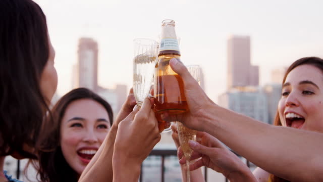 Nahaufnahme-von-Freunden-mit-Getränken-machen-einen-Toast-auf-Dachterrasse-mit-Skyline-der-Stadt-im-Hintergrund