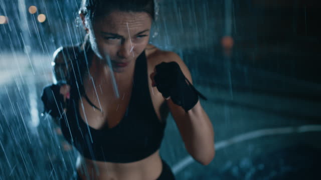 Hermosa-chica-Fitness-deportivo-es-haciendo-ejercicios-de-Sharowboxing.-Ella-está-haciendo-un-entrenamiento-en-la-noche-en-lluvia-pesada-con-una-luz-detrás-de-ella.