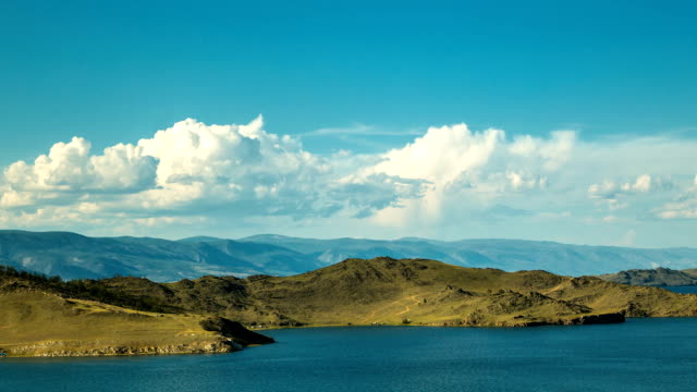 White-clouds-float-above-the-smooth-lake-and-mountainous-terrain.-Cloudscape.