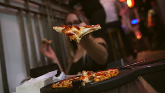 mujer-caucásica-disfrutando-de-cheesy-pizza-en-un-puesto-de-comida-de-la-tarde-en-la-noche