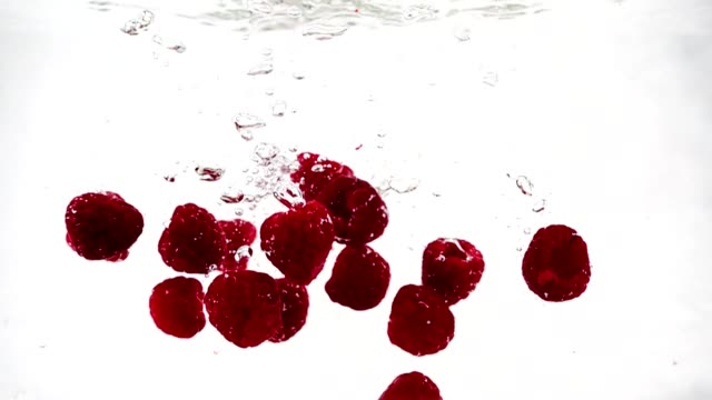 A-ripe-raspberry-falls-into-the-water-with-a-lot-of-small-bubbles.-Video-of-berry-on-isolated-white-background