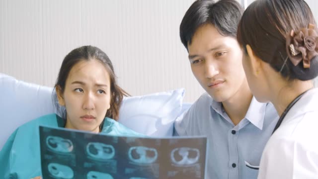 Doctor-showing-X-ray-scan-results-to-pregnant-woman-and-her-husband-with-serious-emotion.-People-with-healthcare-and-medical-concept.