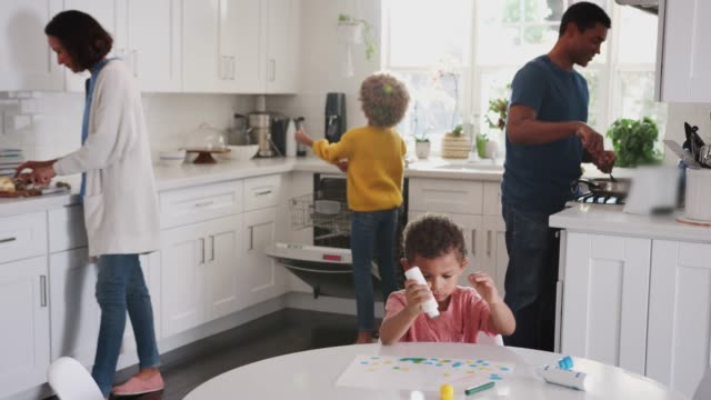 Junge-schwarze-Junge-malen-ein-Bild-in-der-Küche,-während-seine-Familie-Essen-im-Hintergrund-zubereitet