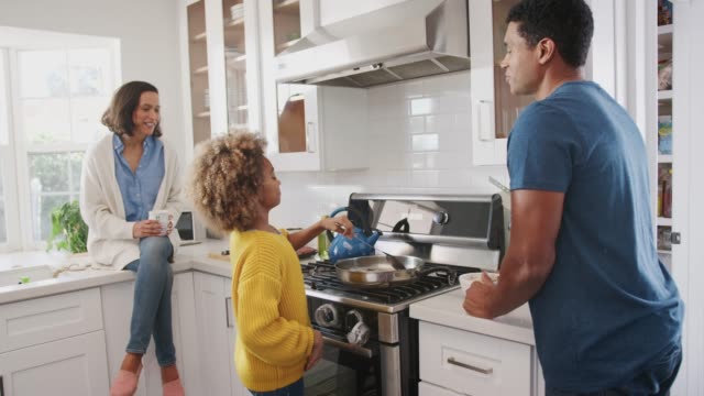 Los-padres-de-raza-mixta-y-su-hija-preadolescente-preparando-comida-juntos-en-la-cocina