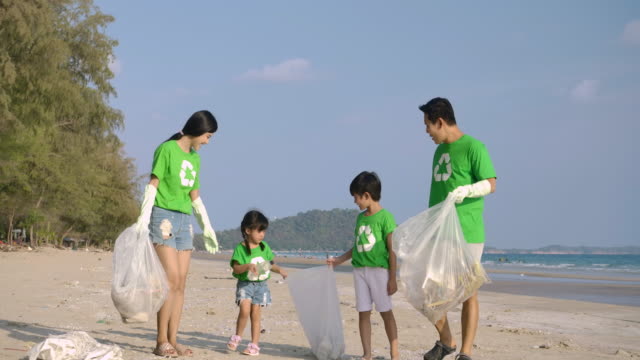 Group-of-volunteers-in-green-t-shirts-cleaning-up-the-beach-with-plastic-bags-full-of-garbage.-Slow-Motion.-Safe-ecology-concept.-4k-resolution.